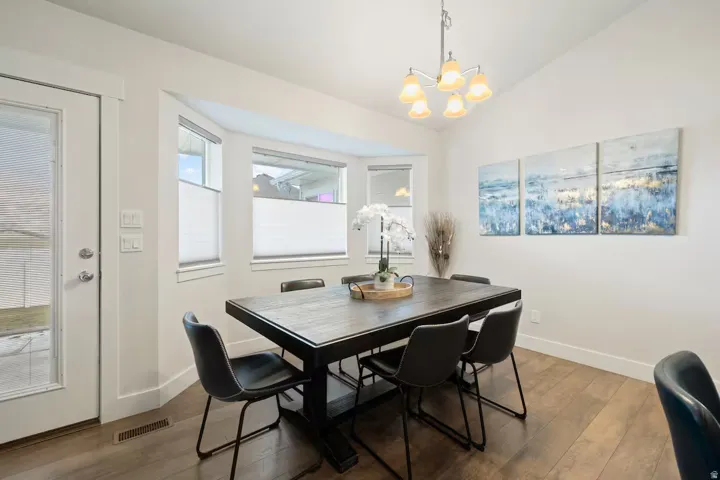 Vaulted ceiling featuring a chandelier, wood-finish flooring, bay window, and a glass-paneled exterior door