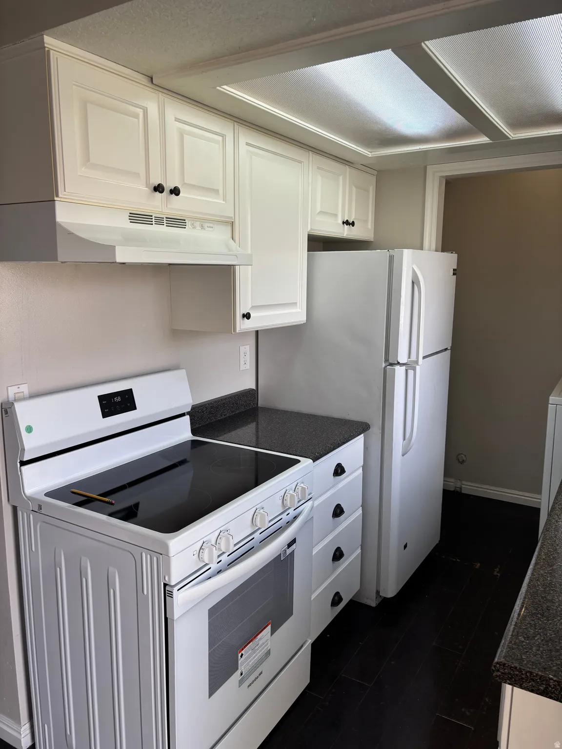 Kitchen featuring white cabinetry, dark countertops, white appliances, and wood-finish flooring