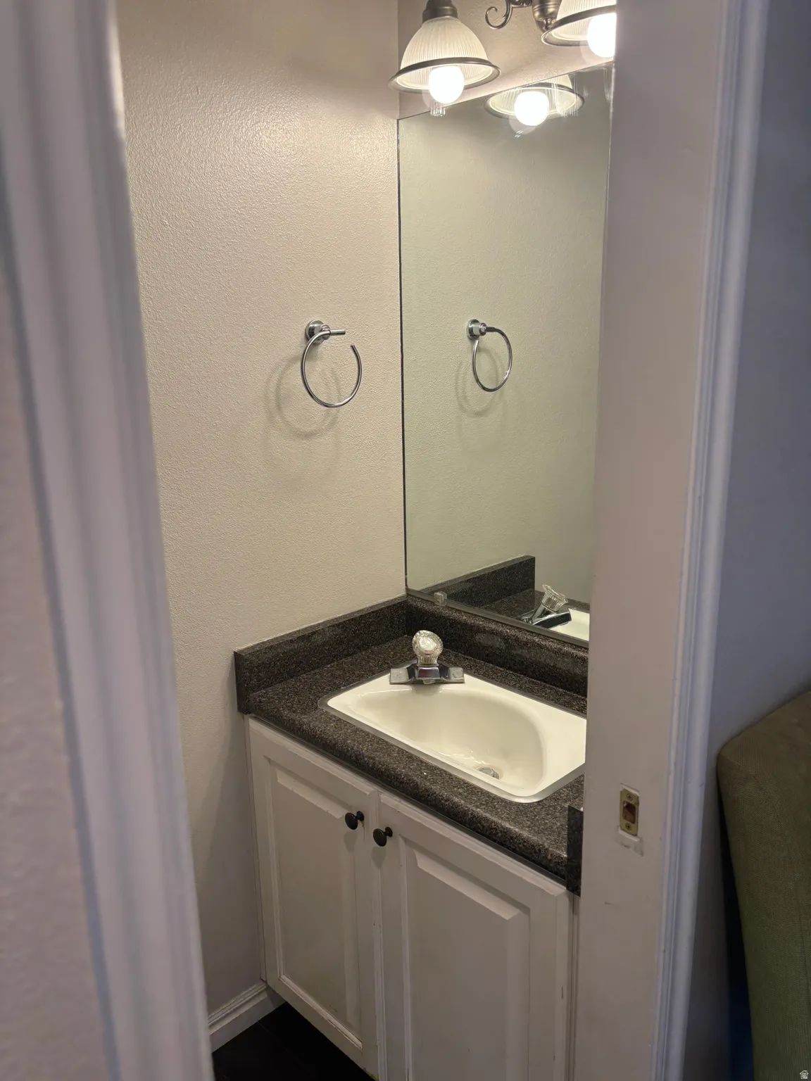 White vanity with dual cabinet doors, integrated sink, and dark countertop