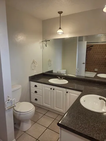 Dual vanity with dark speckled countertops, white cabinetry with dark hardware, large wall-mounted mirror, and tile flooring