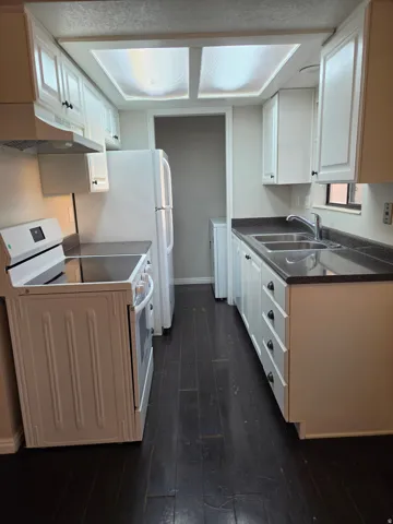 Galley kitchen featuring white cabinetry, dark countertops, a double basin sink, and dark wood-finish flooring