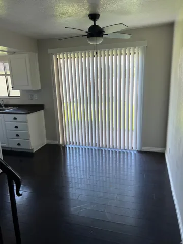 Dark wood-finish flooring, white cabinetry with dark pulls, dark countertops, ceiling fan with integrated lighting, and vertical blinds