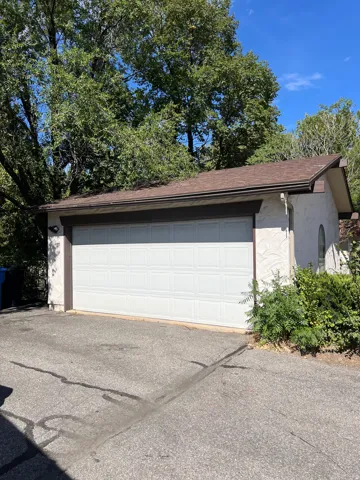 Attached garage with a white panel door, stucco exterior, and sloped shingle roof