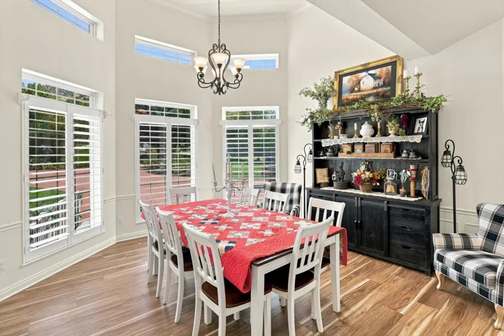 Vaulted ceiling, wood-finish flooring, contemporary chandelier, white plantation shutters, and extensive crown molding