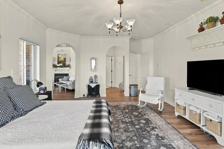 Wood-finish flooring throughout, crown molding, arched doorways, and a classic chandelier