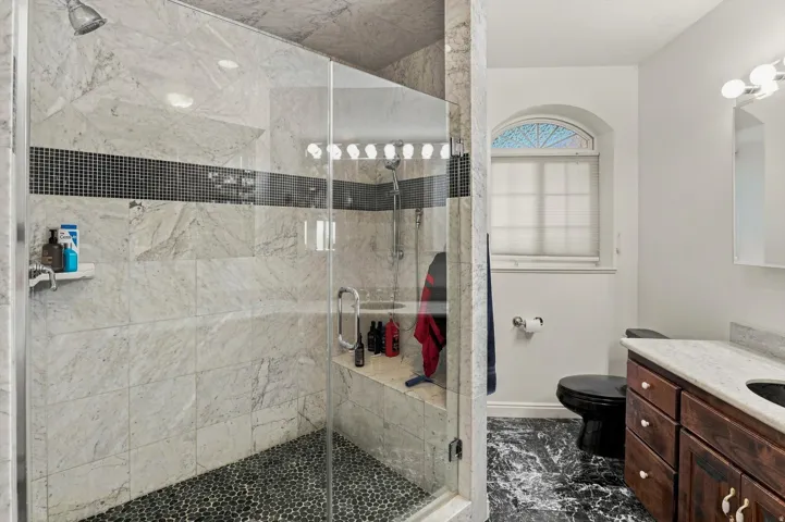 Glass-enclosed shower with stone tile walls, pebble floor, and integrated bench