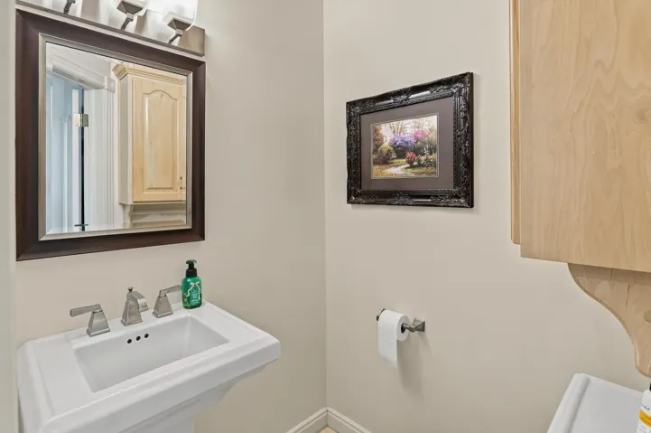 Pedestal sink with a brushed nickel faucet, framed mirror, and integrated vanity lighting