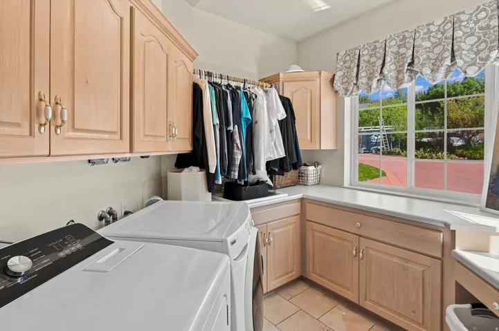 Laundry room with wood-finish cabinetry, light-colored countertops, large window, and tile flooring