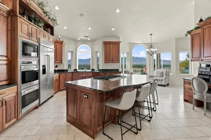 Spacious kitchen featuring warm wood cabinetry, stainless steel appliances, a large center island with counter seating, dark countertops, and arched windows