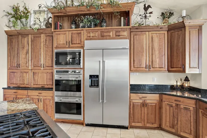 Custom wood cabinetry, stainless steel double oven, built-in microwave, stainless steel refrigerator, and dark stone countertops