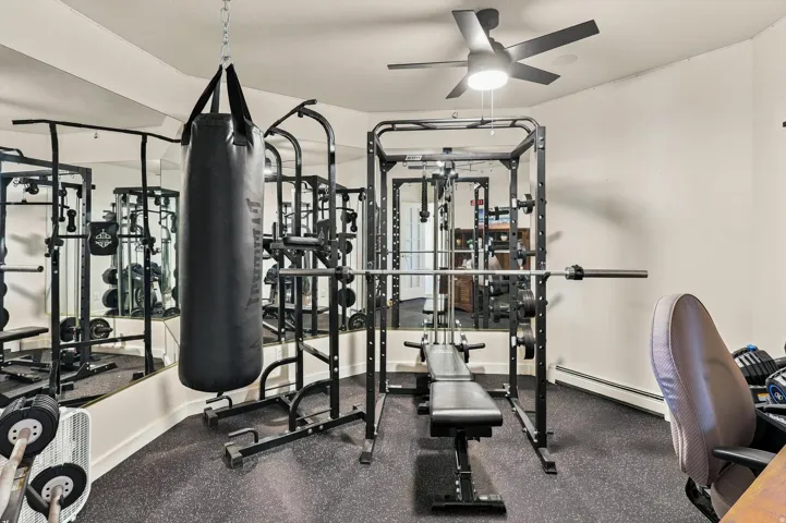 Dedicated exercise space featuring durable rubber flooring, ceiling fan with integrated lighting, and mirrored wall