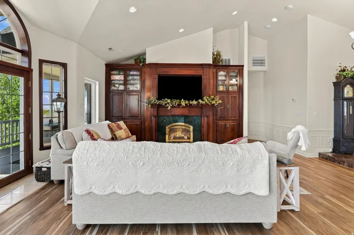 Vaulted ceiling, wood-finish flooring, built-in media cabinetry, fireplace with a green stone surround, and arch-top glass panel doors