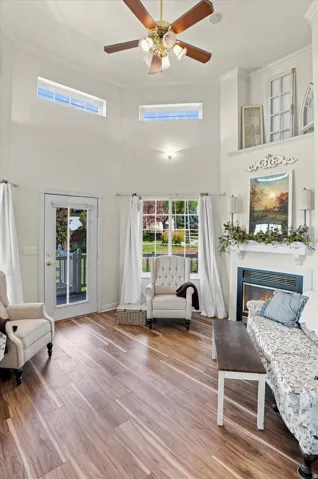 Vaulted ceilings with a ceiling fan, wood-finish flooring, a glass-paneled exterior door, and a built-in fireplace with a mantel
