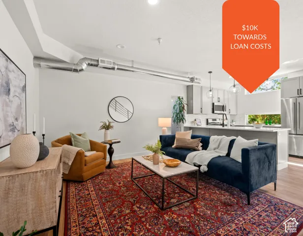 Open-concept living space featuring high ceilings with exposed metallic ductwork, light-toned cabinetry, a quartz-topped island with an integrated sink, stainless steel appliances, and wood-finish flooring