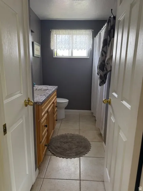 Bathroom featuring a light wood-finish vanity with a granite-style countertop, white toilet, and tile flooring