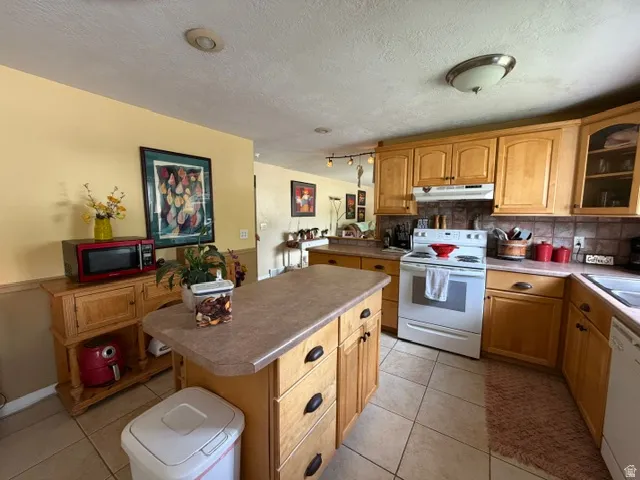 Kitchen featuring wood-finish cabinetry, a central island with countertop, tile flooring, and a tile backsplash