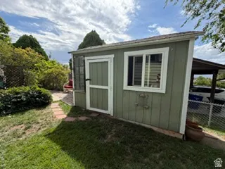 Green-painted storage shed with a shingle roof, white-framed window, and a white-framed door