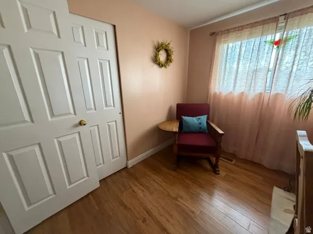 Wood-finish flooring, white paneled closet doors with brass hardware, and a window with sheer drapes