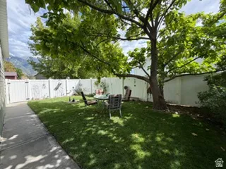 Private yard space featuring a manicured lawn, mature shade trees, and a white privacy fence