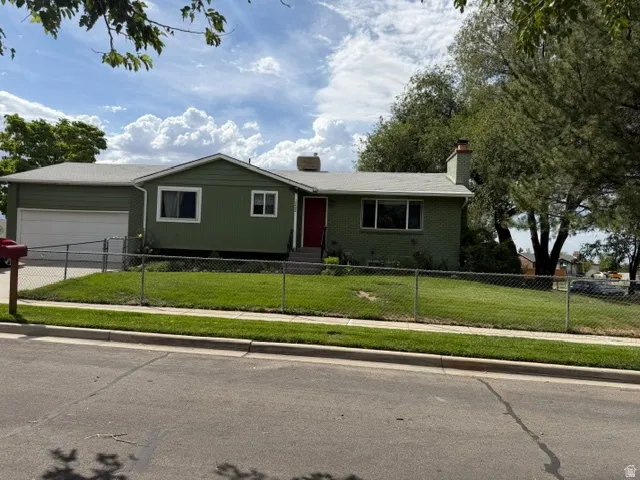 Single-story residence featuring a two-car garage, a chain-link fence enclosing the front yard, and a red entry door