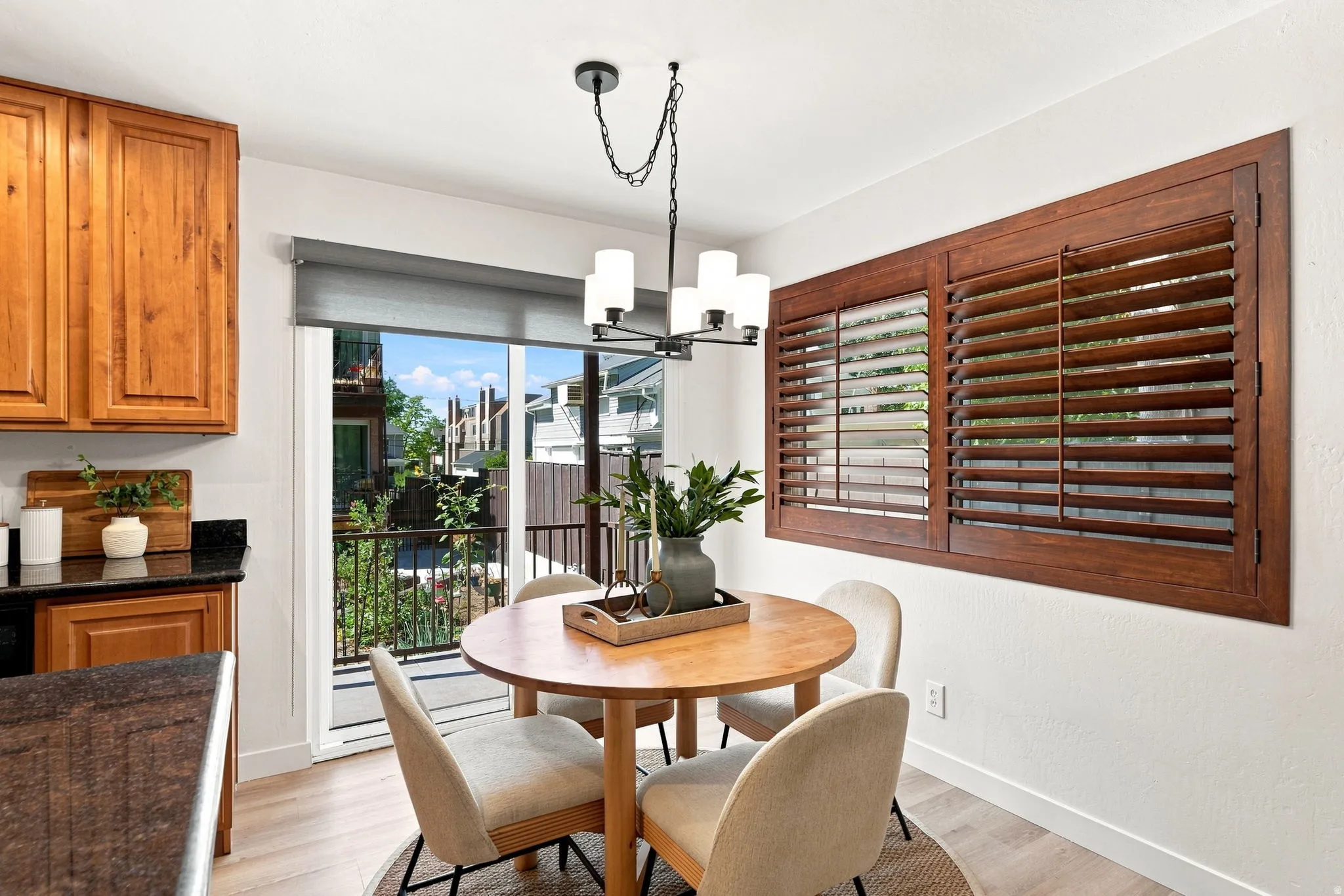 Wood-finish flooring, dark wood plantation shutters, black granite-style countertops, wood cabinetry, and a sliding glass door to a balcony