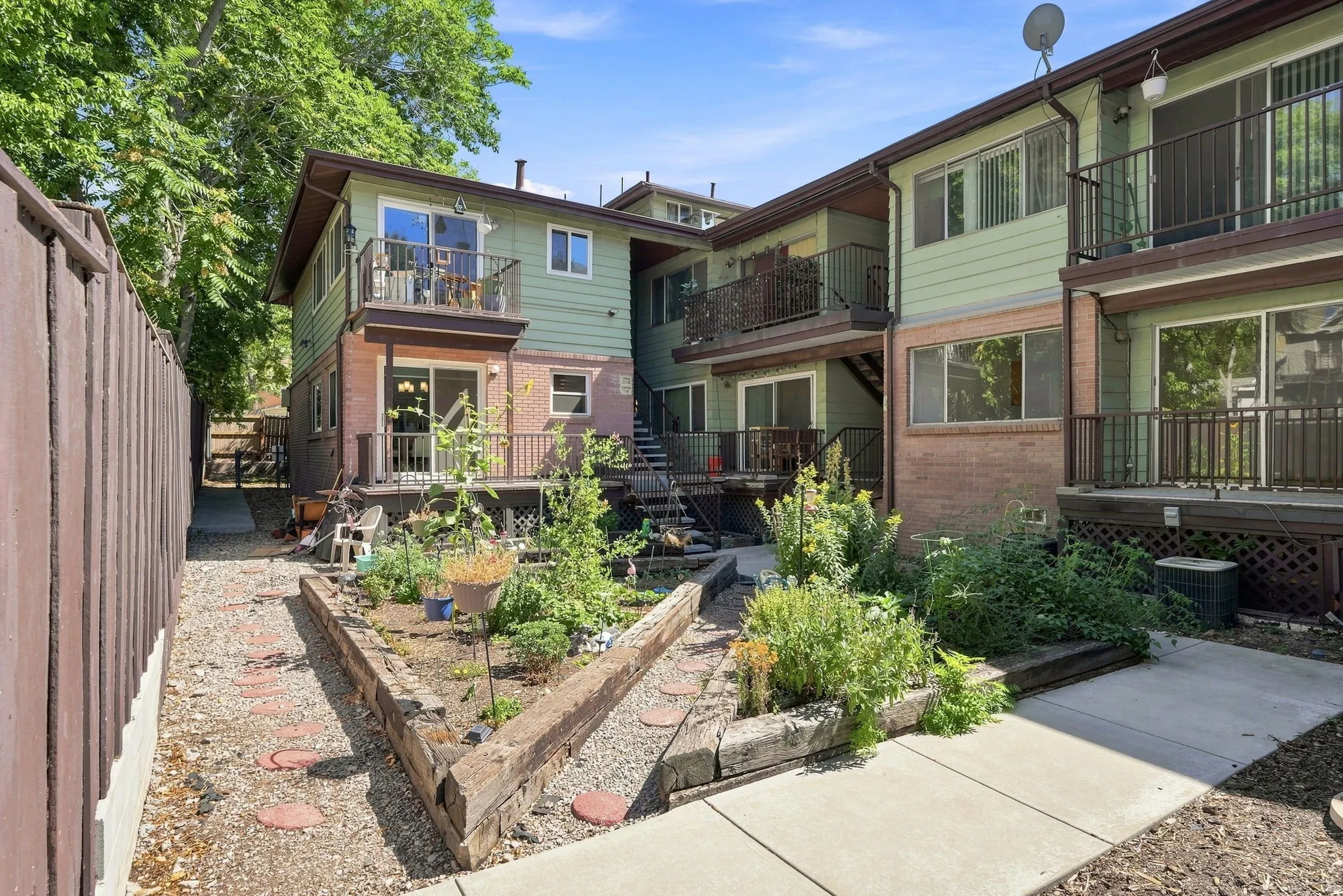 Multi-level exterior with brick and siding, featuring multiple balconies with metal railings, sliding glass doors, and a landscaped garden area with raised beds and stepping stones