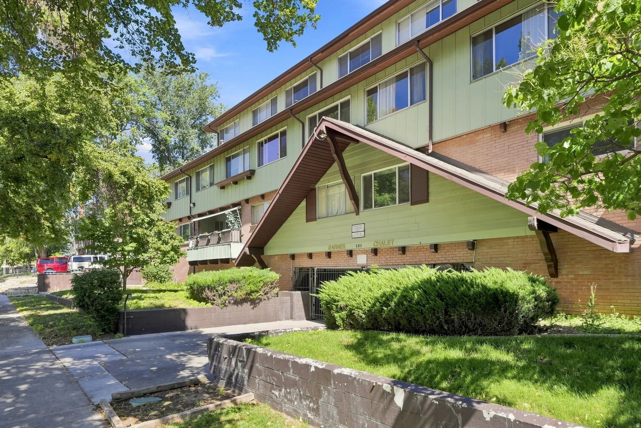 Multi-story building featuring brick and horizontal siding, with a covered entryway and mature landscaping
