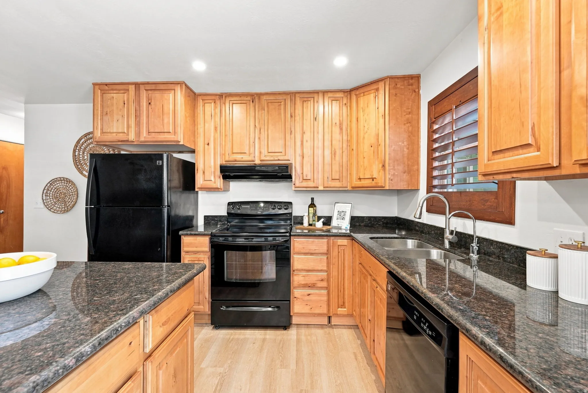 Kitchen featuring wood cabinetry, dark countertops, black appliances, a stainless steel sink, and wood-finish flooring