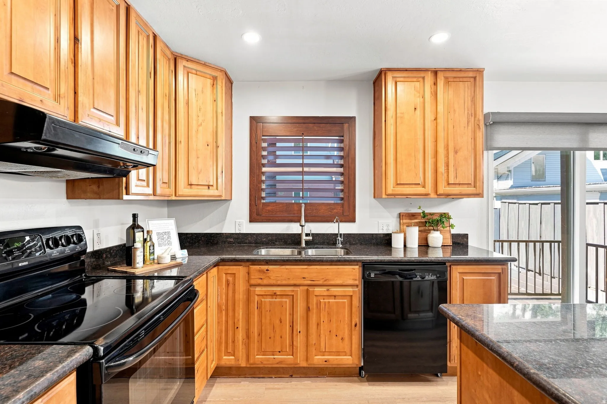 Kitchen featuring wood cabinetry, dark countertops, black appliances, recessed lighting, and a stainless steel sink