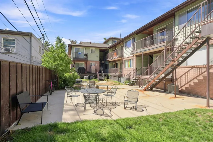Multi-story building exterior with individual balconies, brick foundation, and exterior stair access