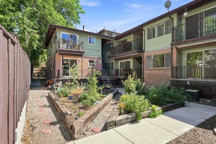 Multi-level exterior with brick and siding, featuring multiple balconies with metal railings, sliding glass doors, and a landscaped garden area with raised beds and stepping stones