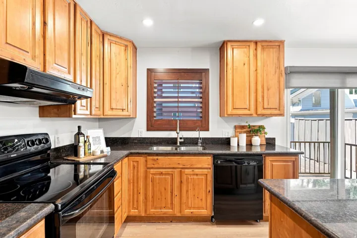 Kitchen featuring wood cabinetry, dark countertops, black appliances, recessed lighting, and a stainless steel sink