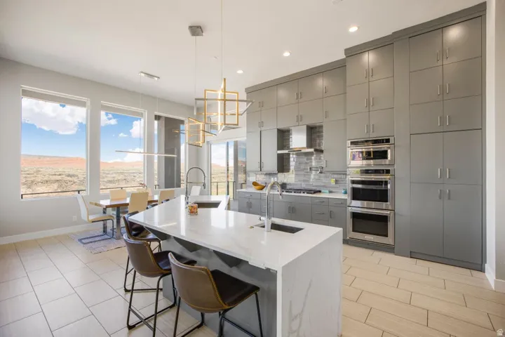 Modern kitchen featuring an expansive island with a waterfall countertop, integrated stainless steel appliances, extensive cabinetry, and large windows