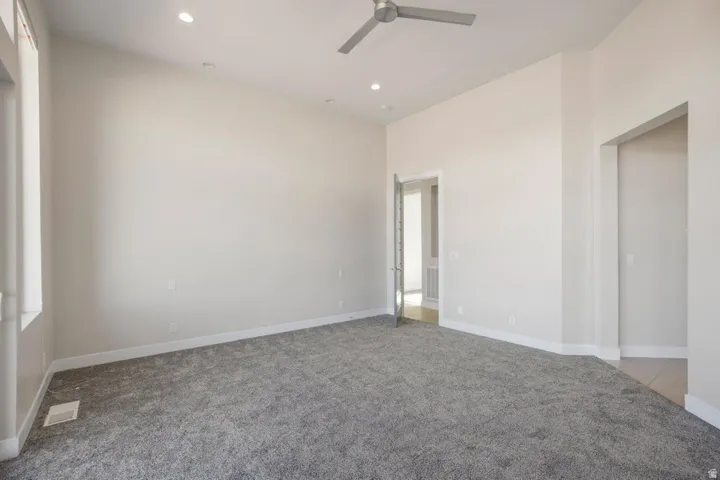 Plush gray carpeting, a contemporary ceiling fan, recessed lighting, and white baseboards