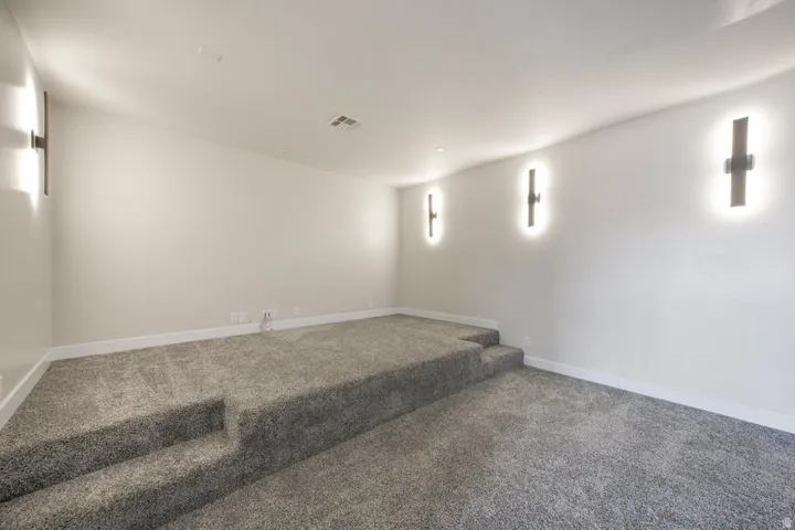 Tiered carpeting with integrated steps, neutral wall paint, and modern wall sconces