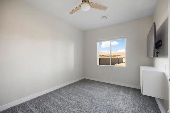 Recessed lighting, wood-finish ceiling fan, neutral wall paint, gray carpet flooring, and a floating white cabinet