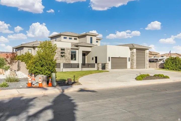 Stucco and stone facade with multiple garage doors, a curved concrete driveway, and varied rooflines