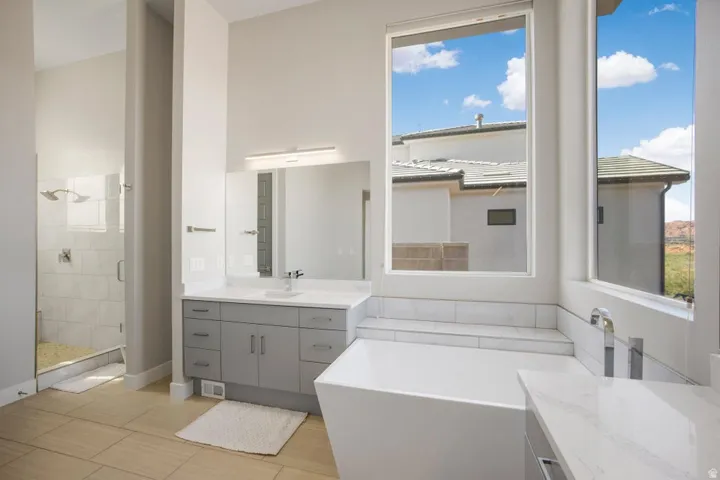 Freestanding soaking tub with tile surround, dual vanity with quartz countertops, wood-finish flooring, and a glass-enclosed shower