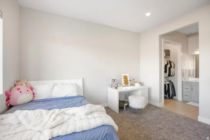 Recessed lighting, light gray carpet flooring, white walls, white trim, and an open doorway to a walk-in closet and bathroom