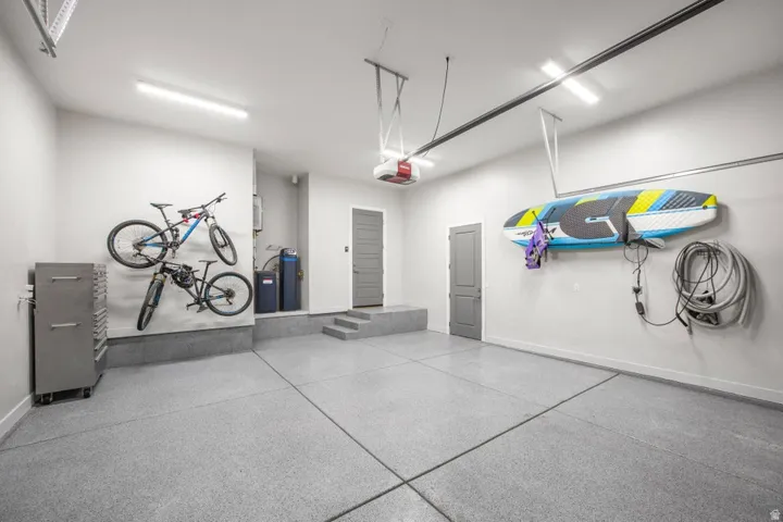 Spacious garage with light grey epoxy flooring, multiple ceiling-mounted light fixtures, and a garage door opener