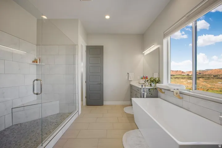 Freestanding soaking tub, glass-enclosed shower with bench, wood-finish flooring, and a vanity with an undermount sink