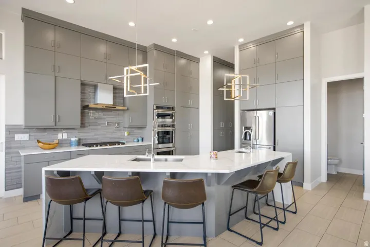 Contemporary kitchen featuring extensive gray cabinetry, integrated stainless steel appliances, a large center island with a built-in sink and seating, and modern pendant lighting