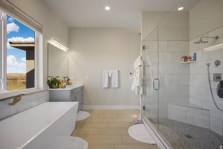 Freestanding soaking tub, frameless glass shower enclosure, wood-finish flooring, dual shower heads, and an integrated shower bench
