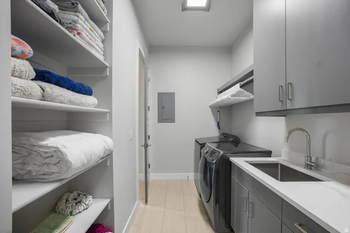 Laundry area featuring wood-finish flooring, built-in shelving, under-cabinet lighting, a utility sink, and light-toned countertops