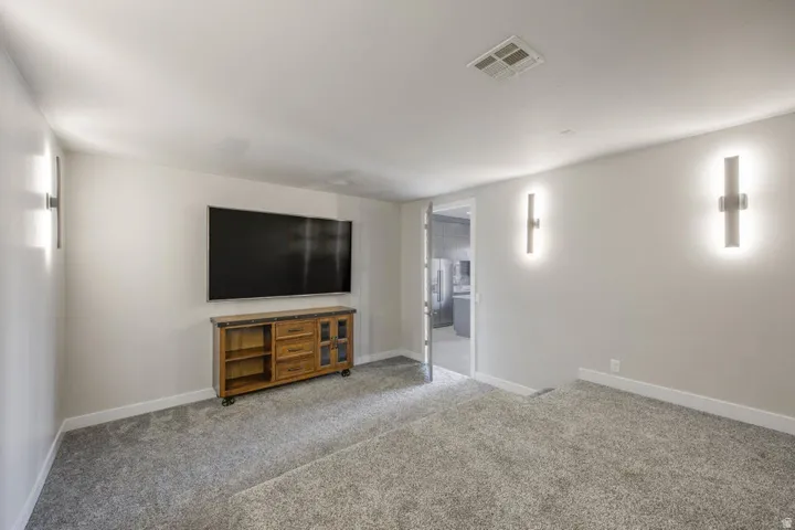 Carpeted interior space with neutral wall tones, modern wall sconces, and recessed ceiling vents