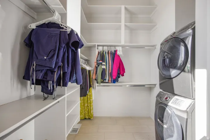 Integrated laundry area with stacked washer and dryer, custom built-in shelving, multiple hanging rods, and wood-finish flooring