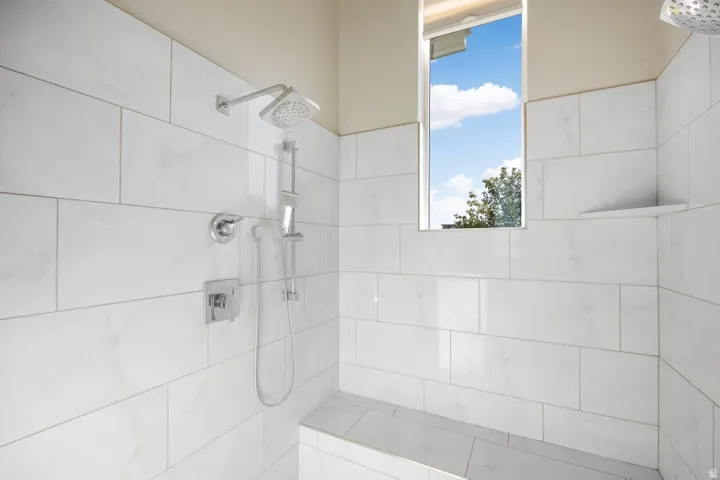 Shower enclosure with white subway tile, a built-in bench, a corner shelf, and a window