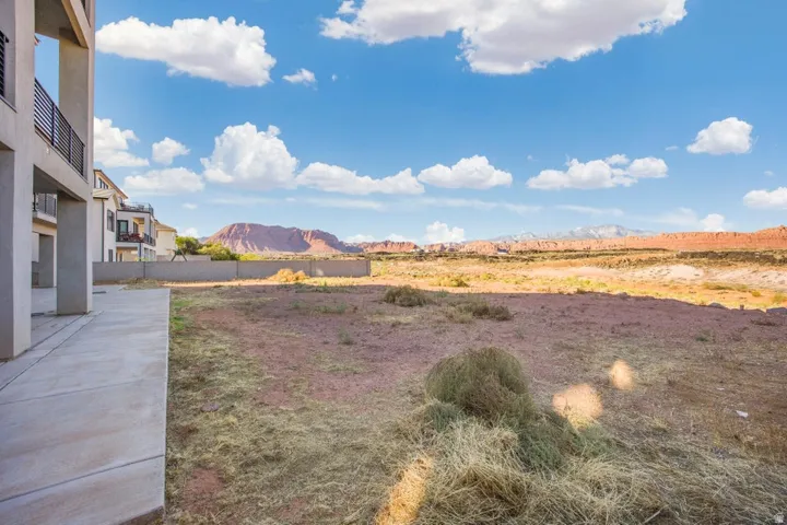 Concrete walkway with adjacent undeveloped land, featuring distant red rock formations and a clear sky