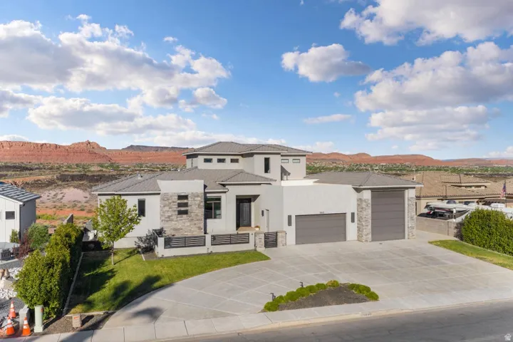 Modern exterior featuring a light gray facade, stone accents, two integrated garages, a concrete driveway, and a manicured lawn