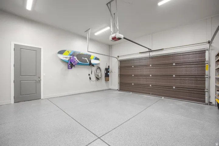 Garage featuring a gray epoxy-coated concrete floor, a brown overhead door with an automatic opener, and overhead strip lighting
